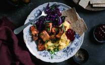 Vegetarisk pinnekjøtt laget av jackfruit servert med kålrotstappe og flatbrød på en blå og hvit tallerken.