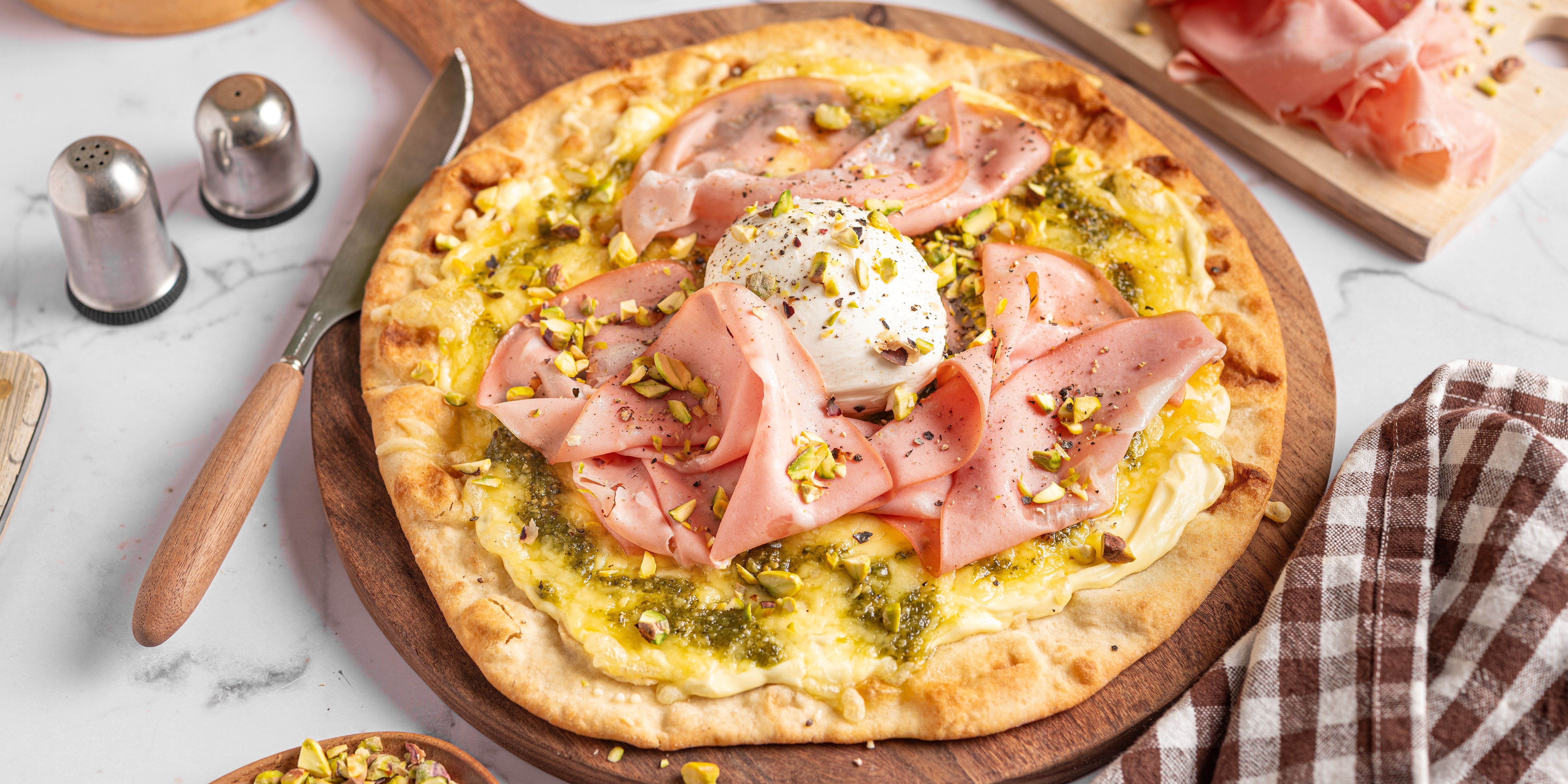 Pizza med skinke, mortadella og en eggeplomme på toppen, servert på et rundt trefat.