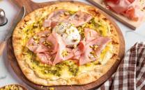 Pizza med skinke, mortadella og en eggeplomme på toppen, servert på et rundt trefat.