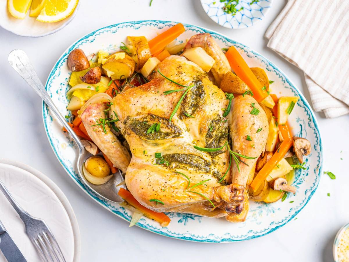 Helstekt kylling med urtesmør og ovnsbakte grønnsaker på et hvitt fat.