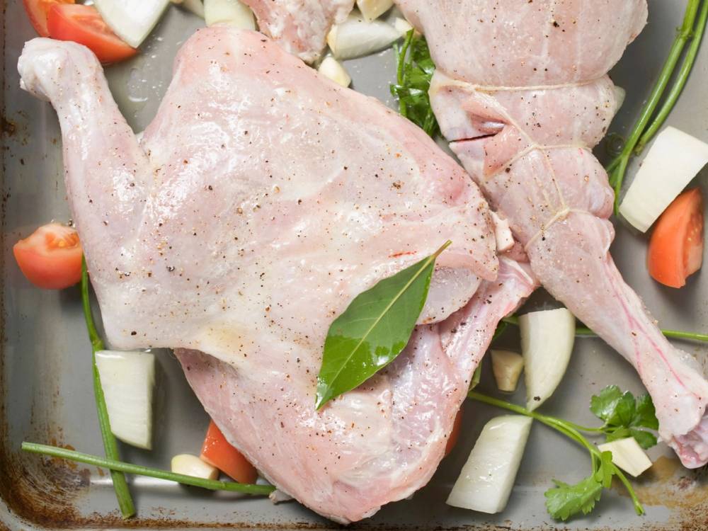 Uskjært rått kyllinglår med urter og grønnsaker rundt på en bakeplate.