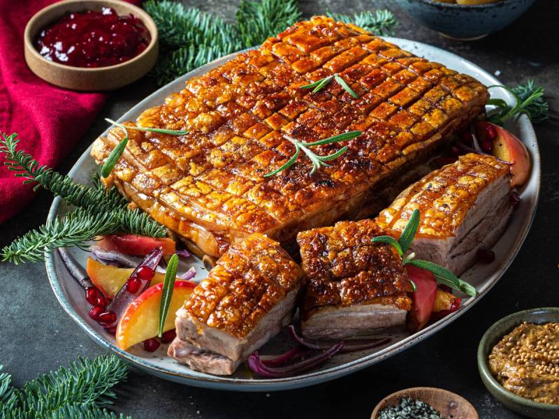 Ribbe med sprø svor, servert med julekrydder og grønne urter på et fat.