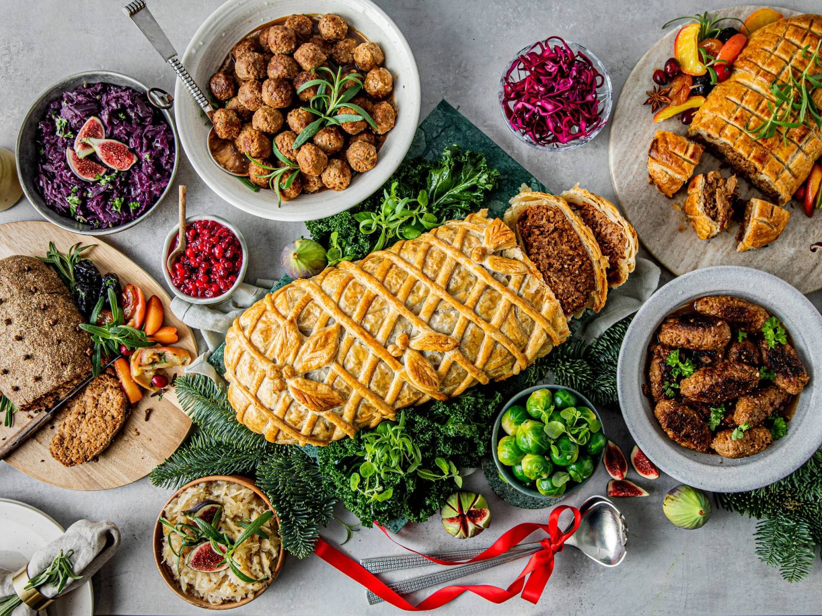 Et bord med julemat, inkludert en stor skinke, grønnsaker, poteter, og ulike tilbehør, pyntet med juledekorasjoner.