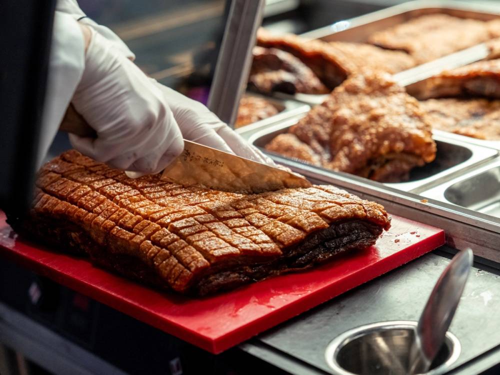 En person skjærer opp store stykker av grillet kjøtt på en matstasjon.