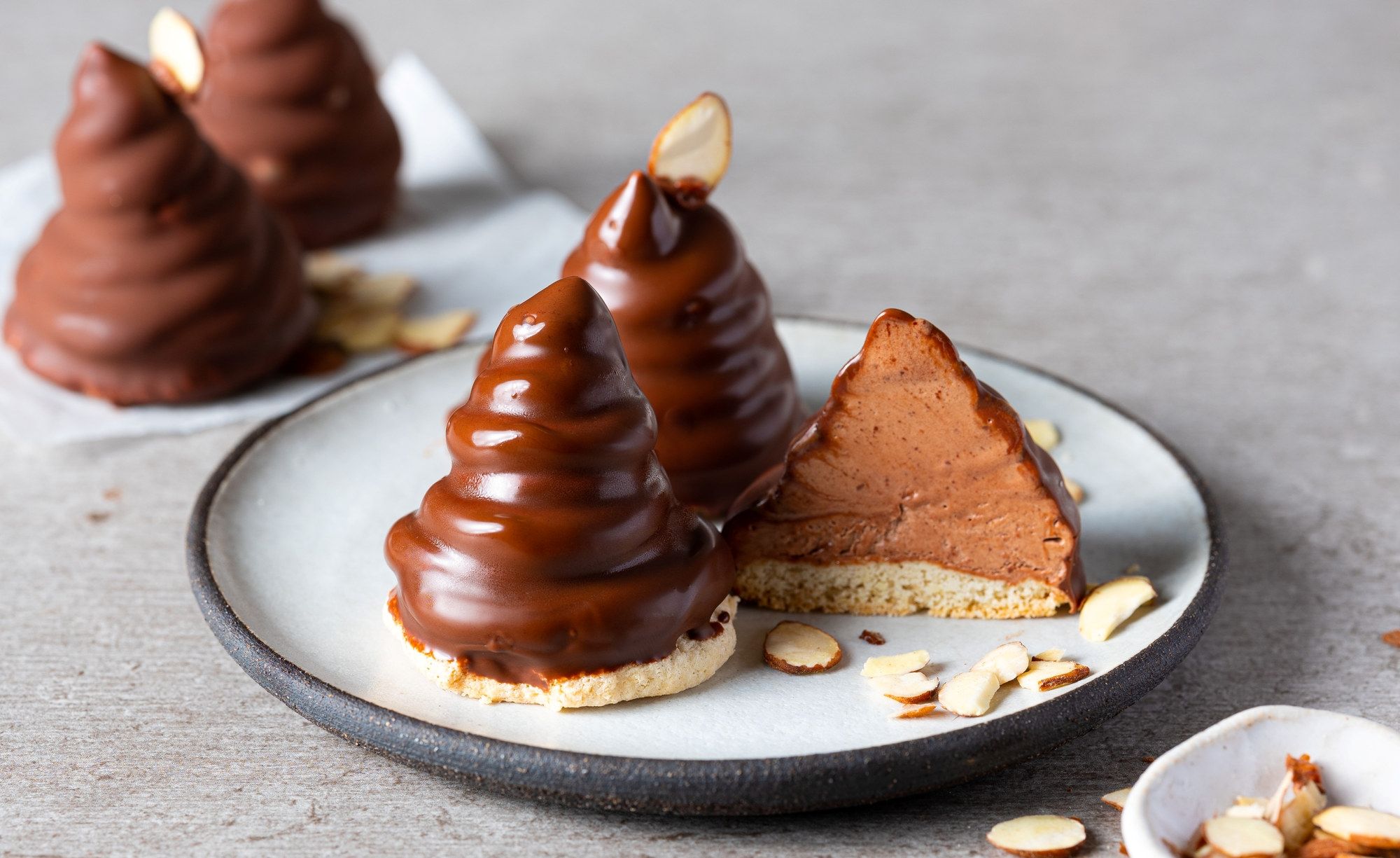 To sjokoladetrær med en kakebit ved siden av på en tallerken, omgitt av mandler og småkaker