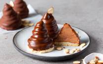 To sjokoladetrær med en kakebit ved siden av på en tallerken, omgitt av mandler og småkaker