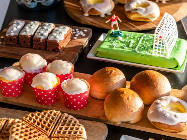 Et utvalg av ulike kaker og bakverk på et bord, inkludert cupcakes, vafler, boller og en marsipankake med fotballtema.