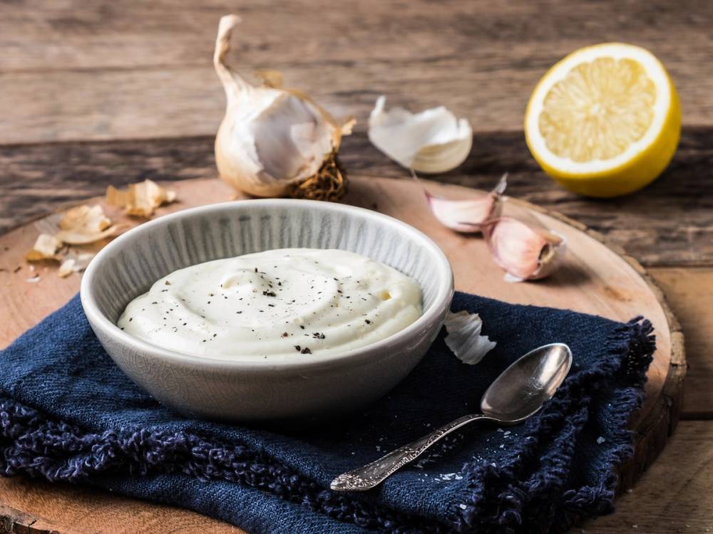 Aioli i en liten bolle med hvitløk, sitron og en skje på et tre- eller trebord