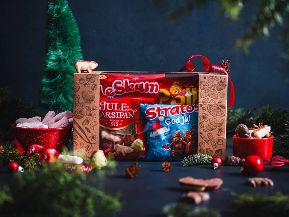 Julegave esker med godteri og små julepynt, plassert på et bord med juledekorasjoner rundt.