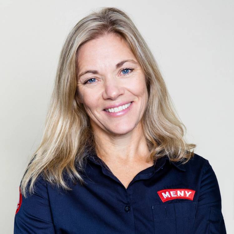 Portrett av Nina Horn Hynne med skulderlangt blondt hår, iført en mørk blå arbeidsuniform med en rød og hvit logo på brystet.