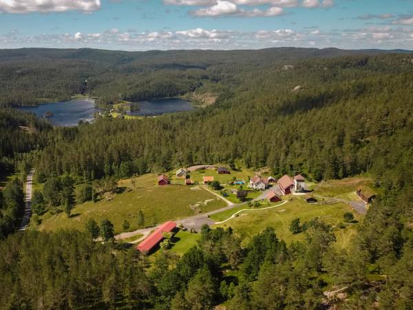 En oversikt over en liten landsby med spredte hus omgitt av grønne skoger og vann i bakgrunnen.