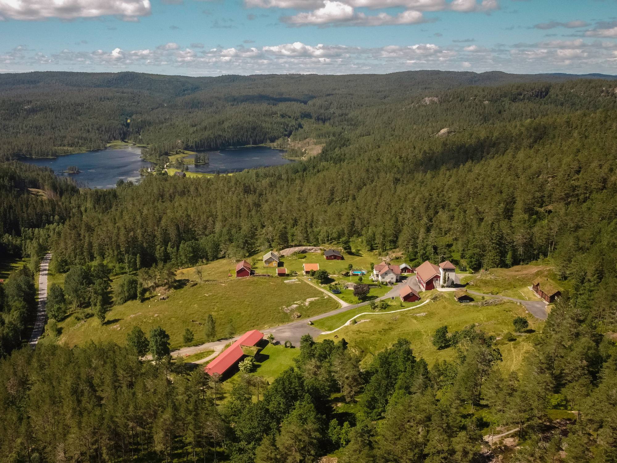 En oversikt over en liten landsby med spredte hus omgitt av grønne skoger og vann i bakgrunnen.
