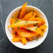 Skål med oppskårne gulrøtter pyntet med finhakket grønt, sannsynligvis persille.