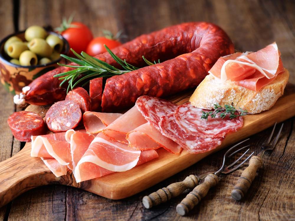 Spekemat med ulike typer tørket og speket kjøtt, oliven og brød på et trefat.