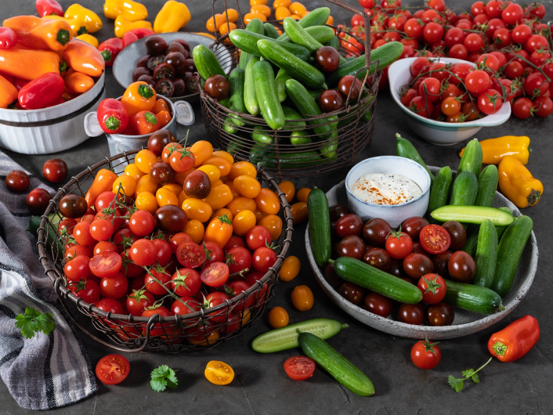 Mini grønnsaker og cherrytomater i ulike farger i små skåler og kurver, med en liten skål med dip i midten.