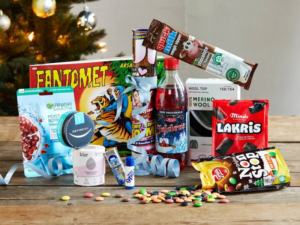 En julekalender med godteri, sjokolade, tyggegummi og en brusflaske, plassert på et bord foran en julegran.