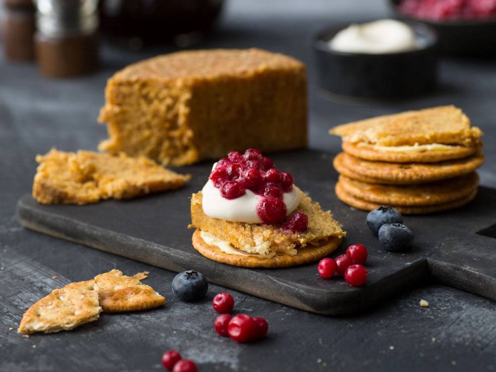 Gamalost på salte kjeks med bær og en skål med rømme i bakgrunnen.
