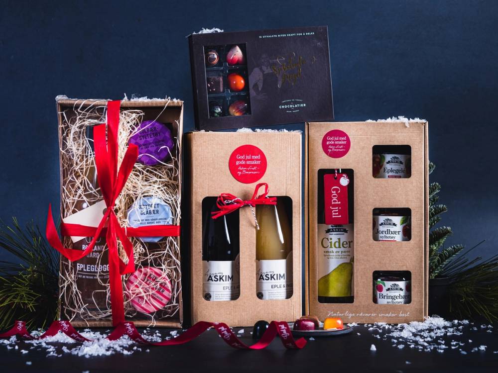 Julegaveesker med matgaver og dekorasjoner på en mørk bakgrunn, med snø på bordet foran.