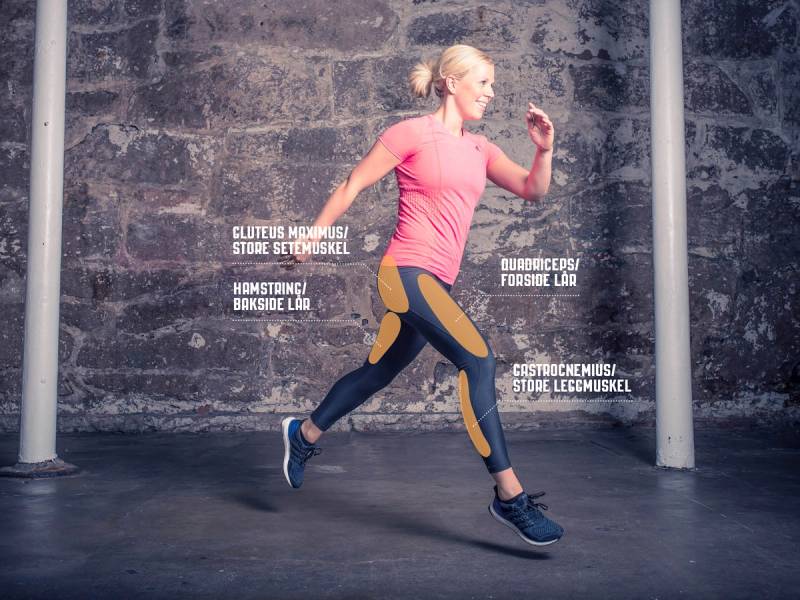 En person i treningstøy løper mot en vegg med tekst om muskelgrupper og trening, sett fra siden.