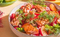 En bolle med en salat av tomater, agurk, urter og sitronbåter, omgitt av glass med drikke og bestikk på et bord.