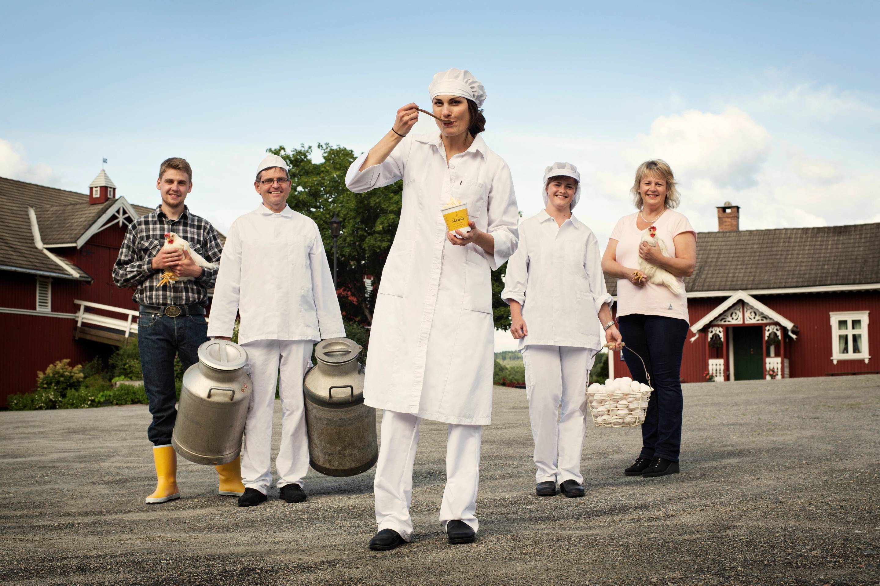 En gruppe mennesker står ute på en gate, med noen i hvite arbeidsklær og en person som holder en kopp, mens de andre smiler og poserer for kameraet.