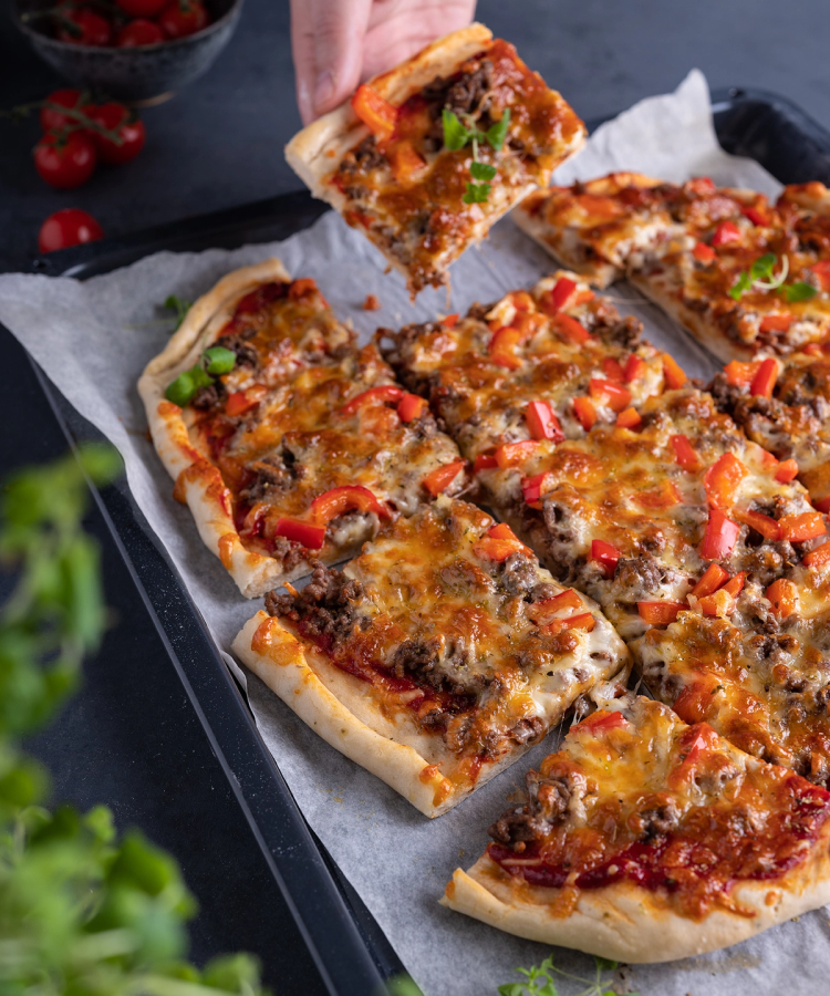 Langpannepizza med kjøttdeig, paprika og ost som er skåret opp og lagt på et stekebrett med bakepapir.