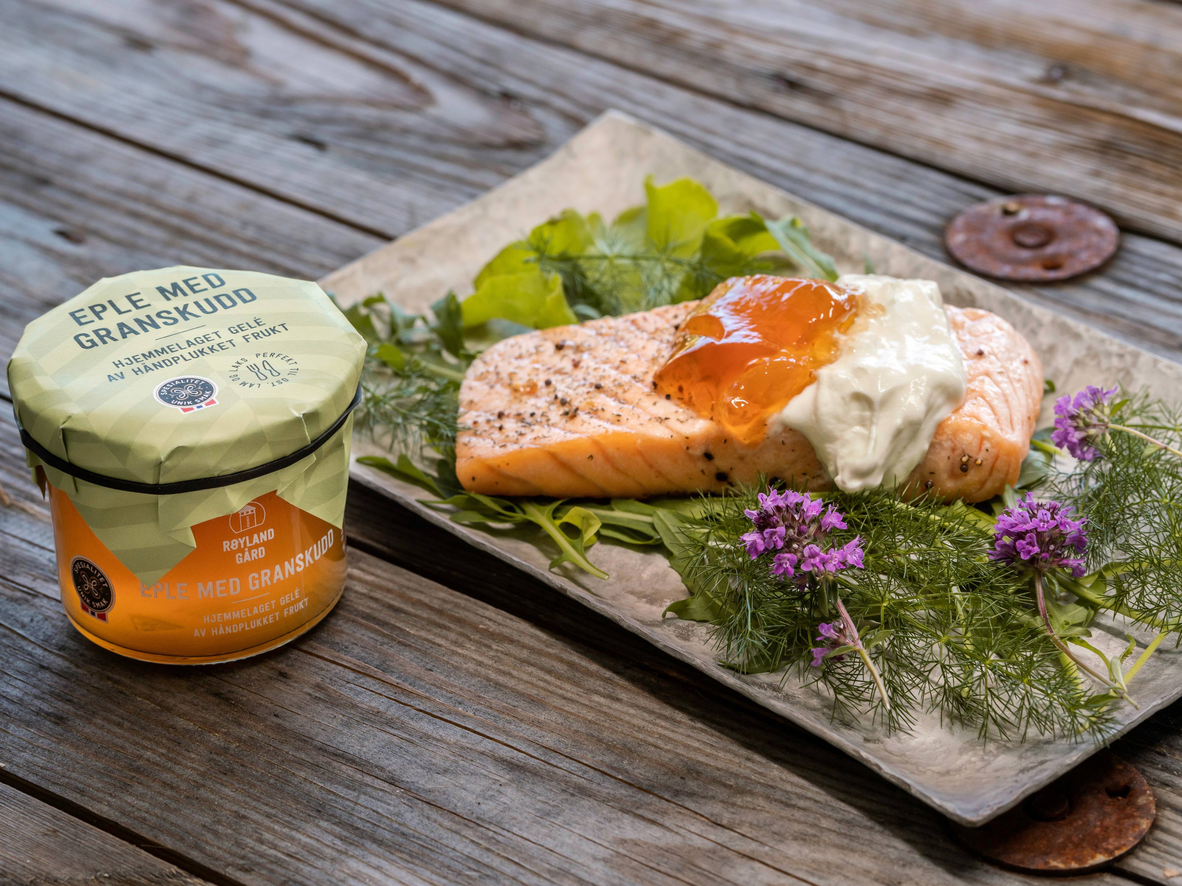 Frokost med laks, eggerøre og en liten salat på en treplate, sammen med en glassmugg med syltetøy.