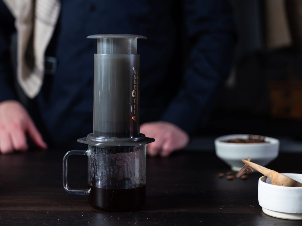 Ferdiglaget kaffe som er presset gjennom en Aeropress, plassert på en svart overflate med en kopp under for å samle opp kaffen.