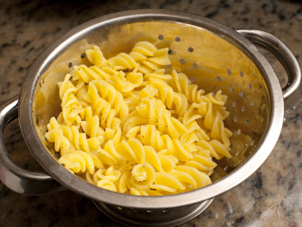 Kokt pasta i en metall-sil med hull, klar til servering.