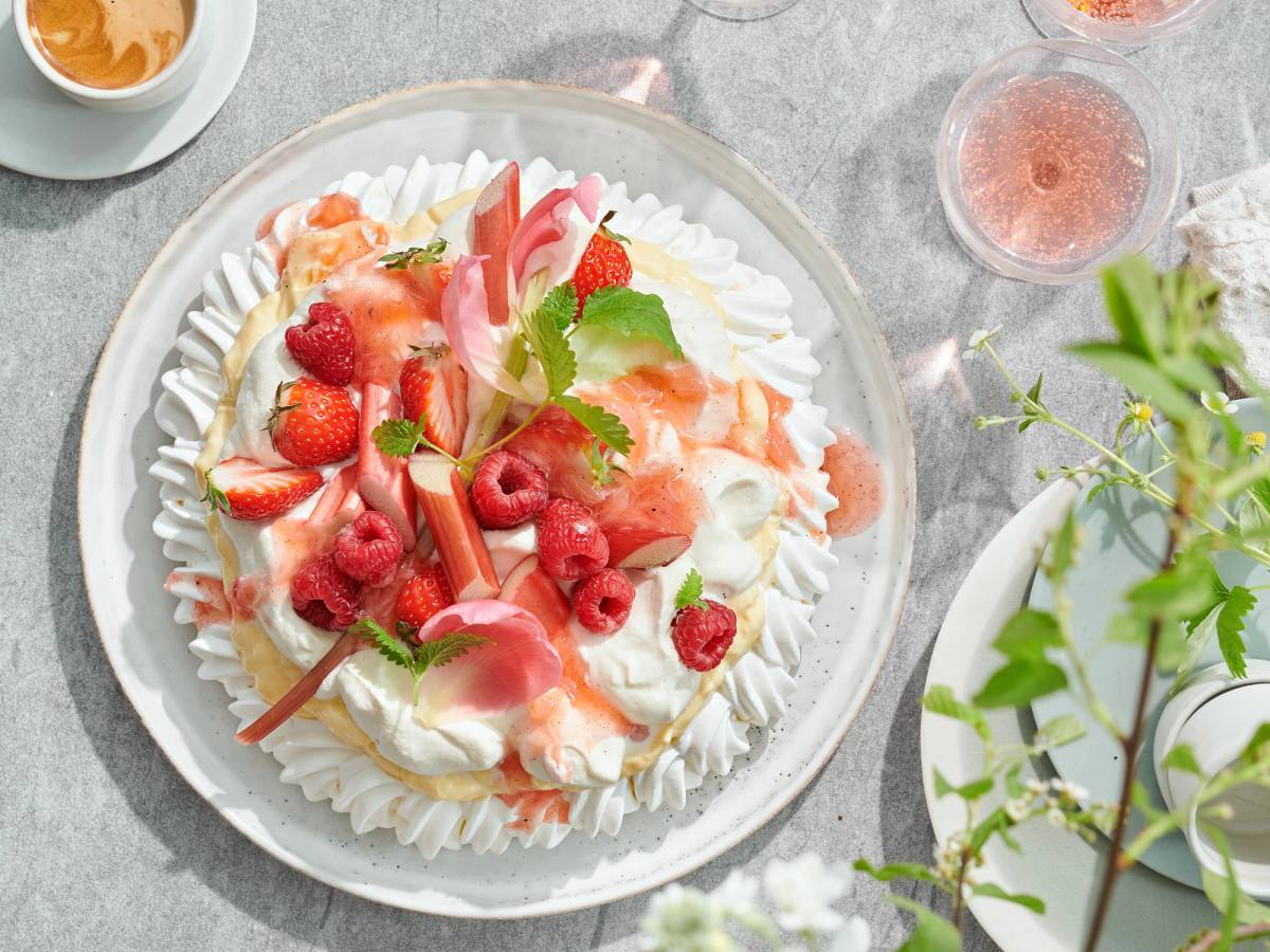 En fristende kake pyntet med friske bær og krem, sett på et bord med kopper og glass rundt.