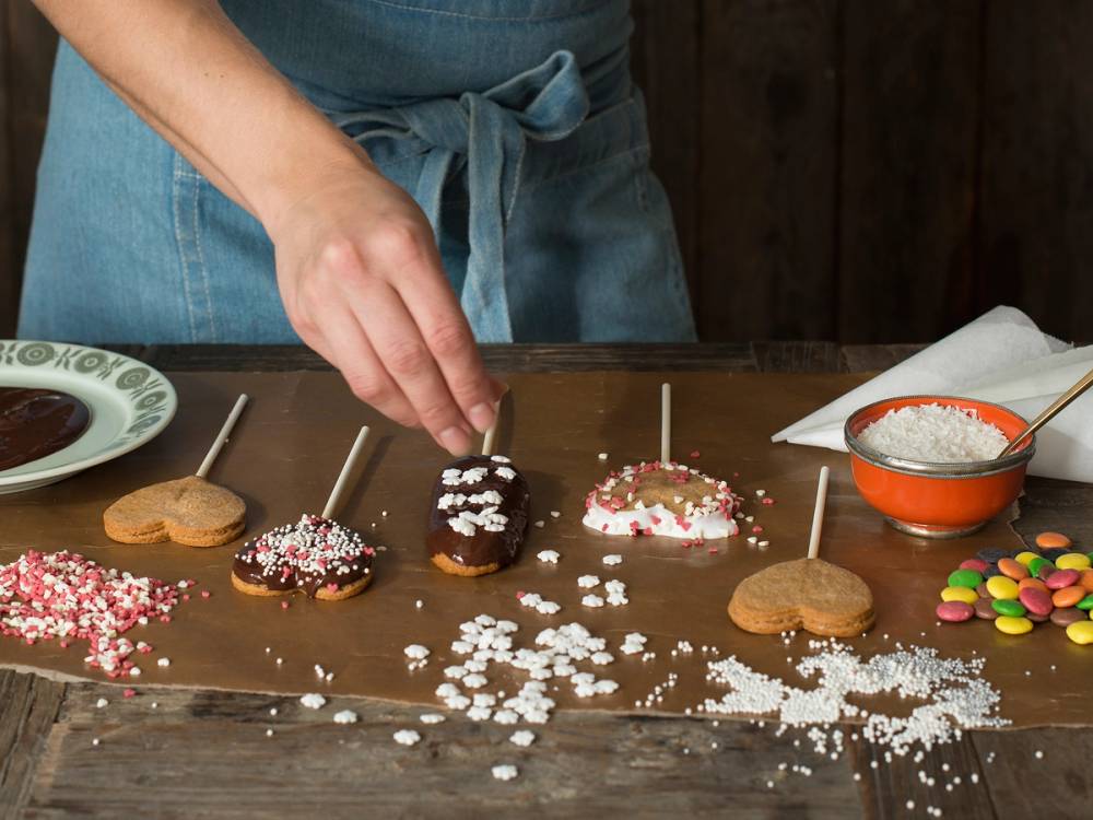 Person dekorerer cupcakes med frosting og strøssel på et kjøkkenbord.