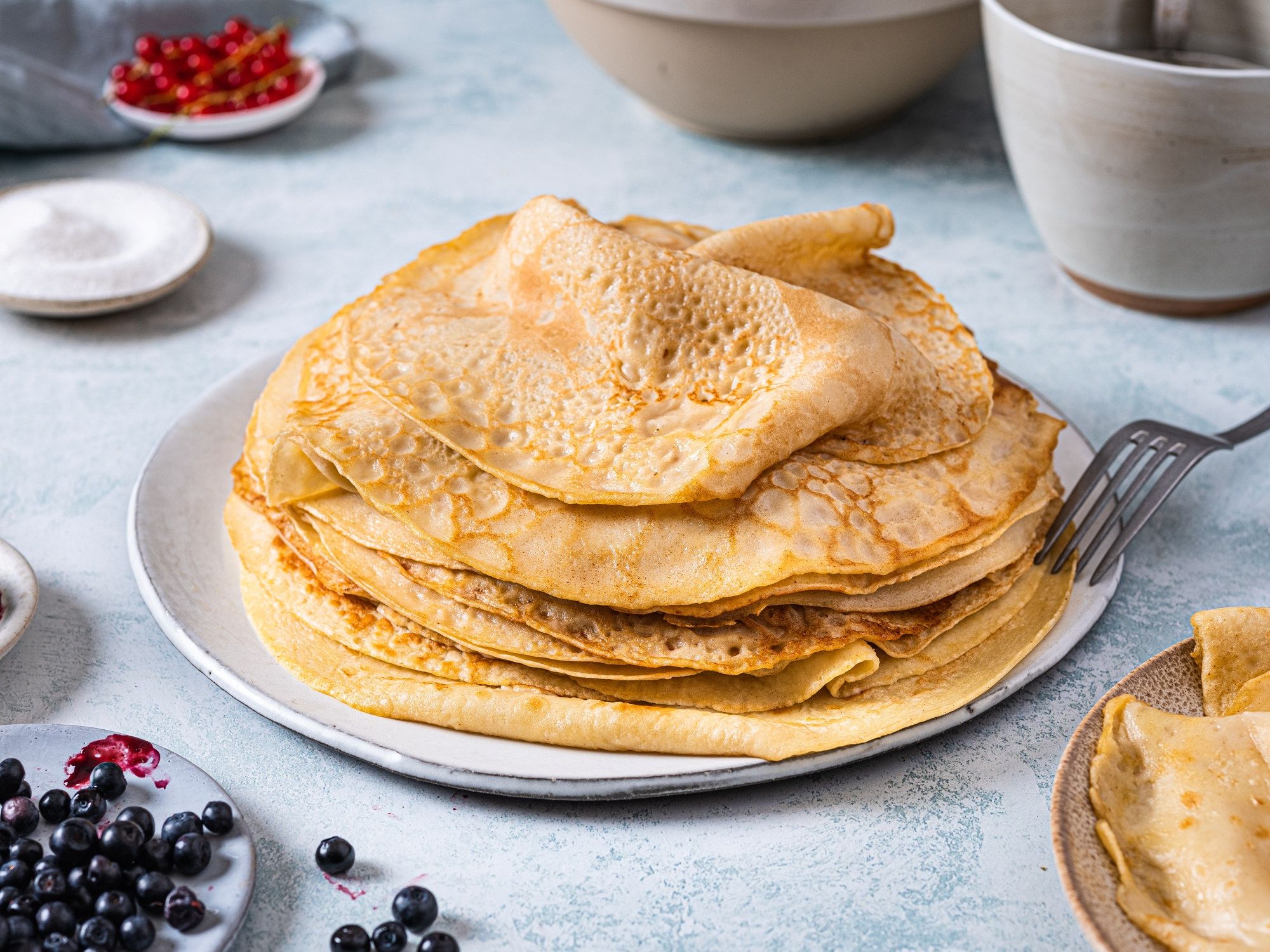 En tallerken med flere tykke pannekaker, servert med bær ved siden av, på et lyst bord.