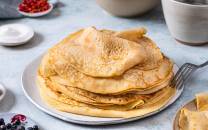 En tallerken med flere tykke pannekaker, servert med bær ved siden av, på et lyst bord.