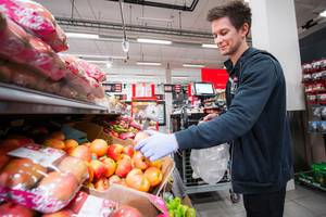 En person handler frukt i en dagligvarebutikk med hyller fylt av ulike frukter og grønnsaker i bakgrunnen.