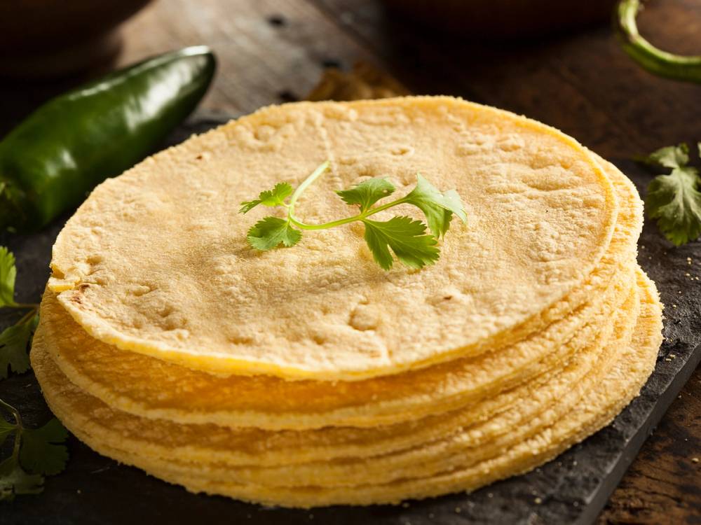 Hjemmelaget glutenfri tortillalefse med en liten kvist koriander på toppen, liggende på en svart tallerken.