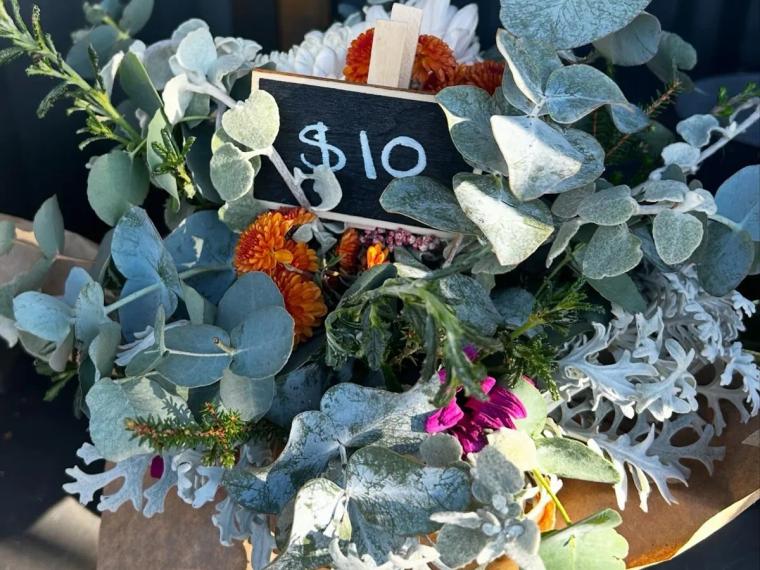 A ten-dollar flower bouquet of eucalyptus, dusty miller and orange and pink chrysanthemums with a small chalkboard price tag, from Hearps Blossom Basket in West Ulverstone