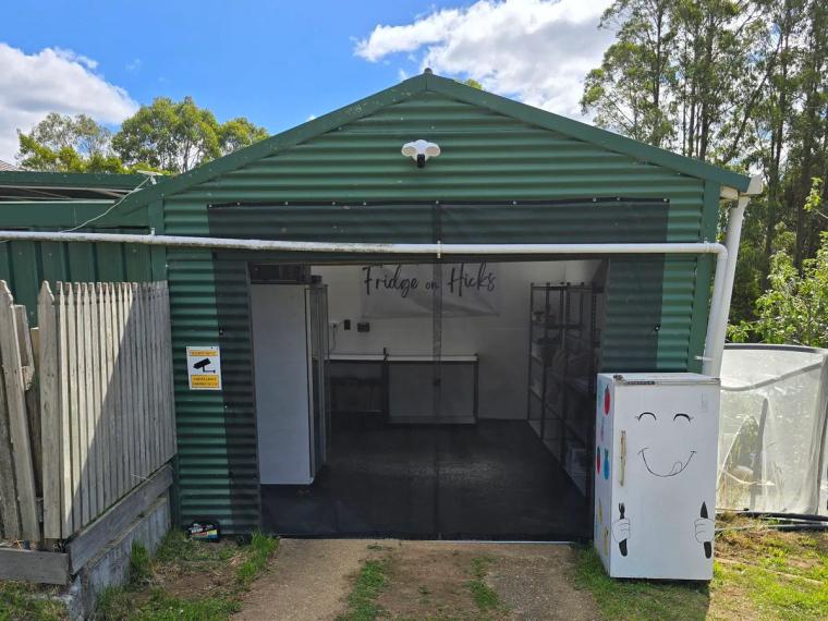 The green corrugated-iron shed at Fridge on Hicks in Yolla, doors open, with a Fridge on Hicks banner inside and a white fridge painted with a smiley face