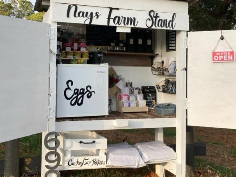 The white timber Nays Farm Stand at Gawler, with a hand-lettered sign, an Eggs bar fridge, a we're open sign and a carton and jar returns box