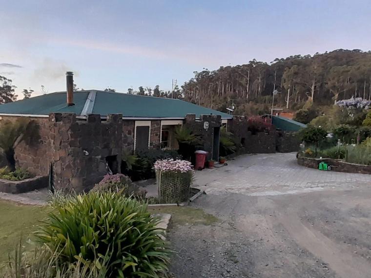 The stone homestead at Chateaux Hamilton Hayes in Underwood, with a green roof, turret-like stonework and a gravel drive against bushland