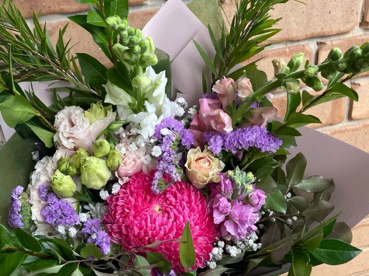 A mixed bouquet from The Petal Porch in Littlehampton, with a pink chrysanthemum, roses, stocks and native foliage against a brick wall