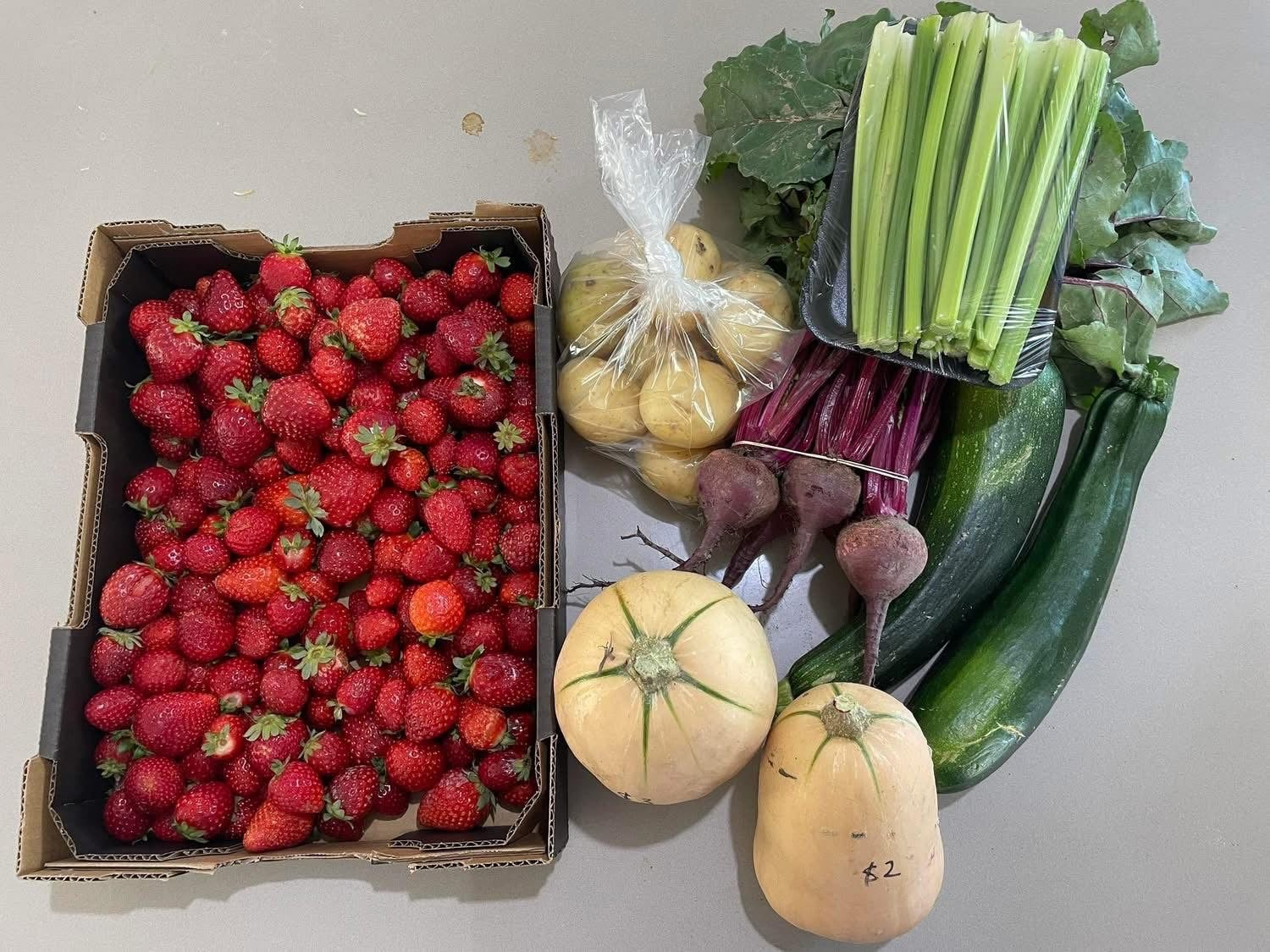 A tray of strawberries beside potatoes, celery, beetroot, zucchini and butternut