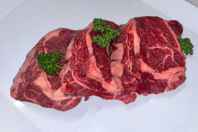Three thick-cut marbled beef steaks with curly parsley on a white bench
