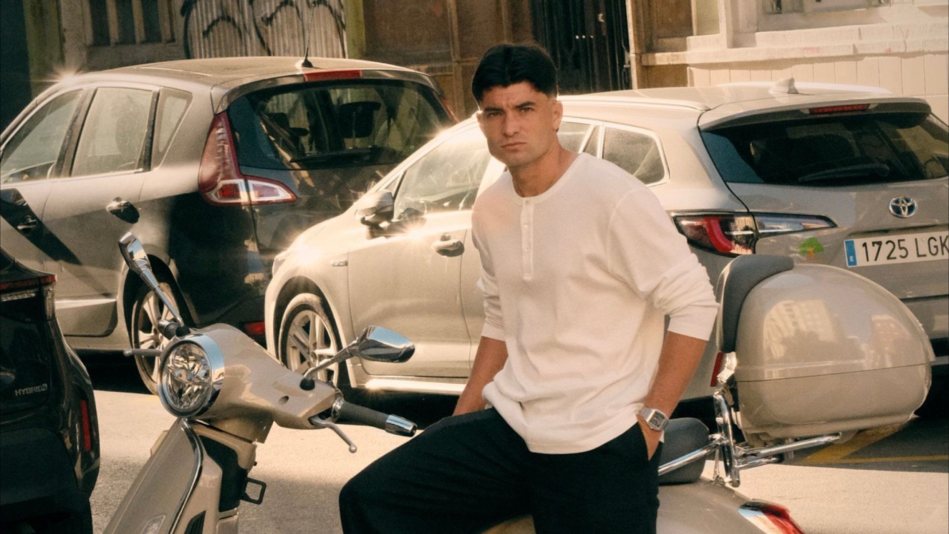 Aritz Aldasoro apoyado en una Vespa en plena calle, con camiseta blanca y pantalón negro, mirando a cámara.