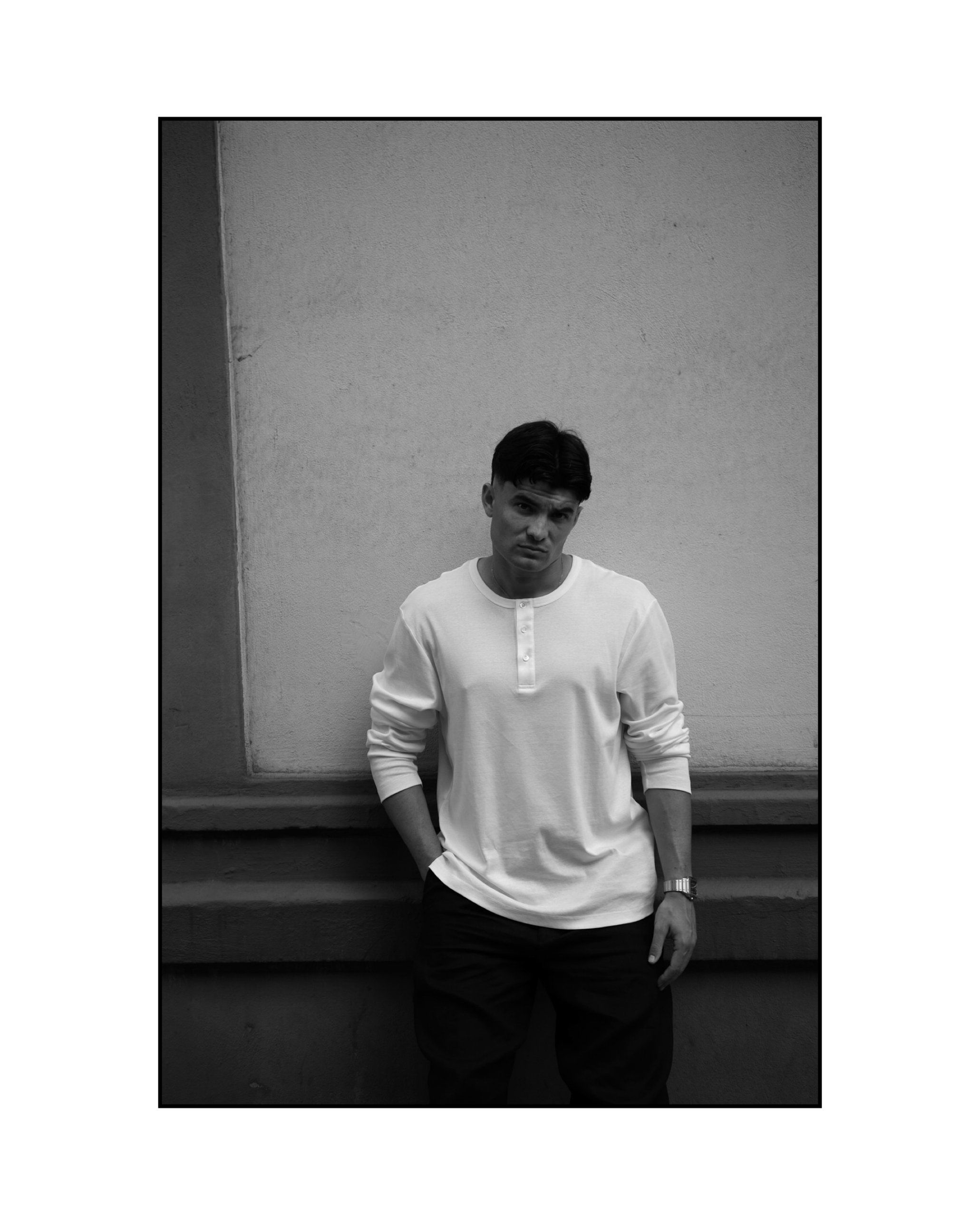 Aritz Aldasoro apoyado en un muro liso con la mano en el bolsillo, en blanco y negro.