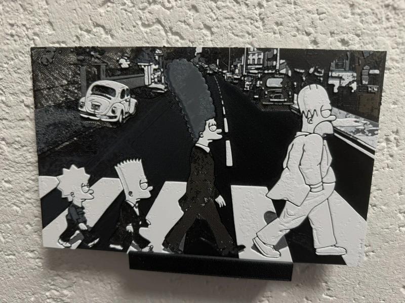 HueForge-Druck an der Wand – die vier Simpsons überqueren in Schwarz-Weiß einen Zebrastreifen im Abbey-Road-Motiv, dahinter ein VW Käfer und eine Straßenzeile