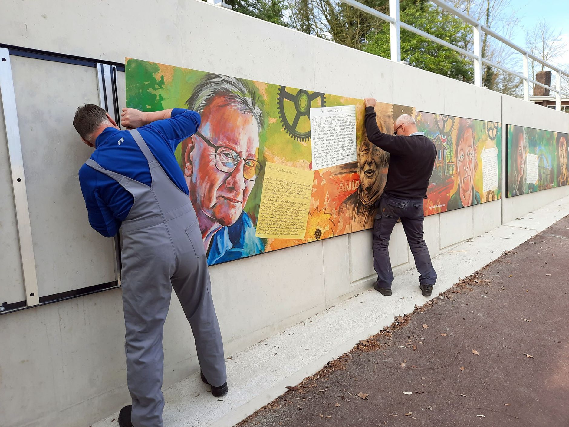 two men are hanging a painting on a wall .