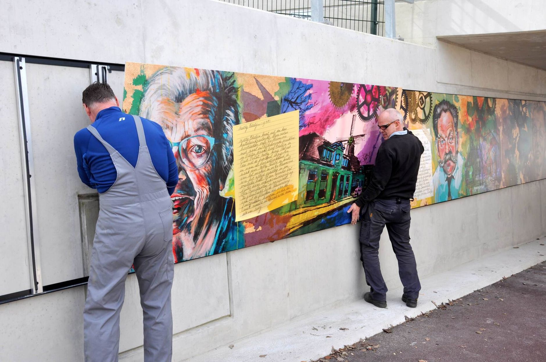 two men are working on a mural on a wall .