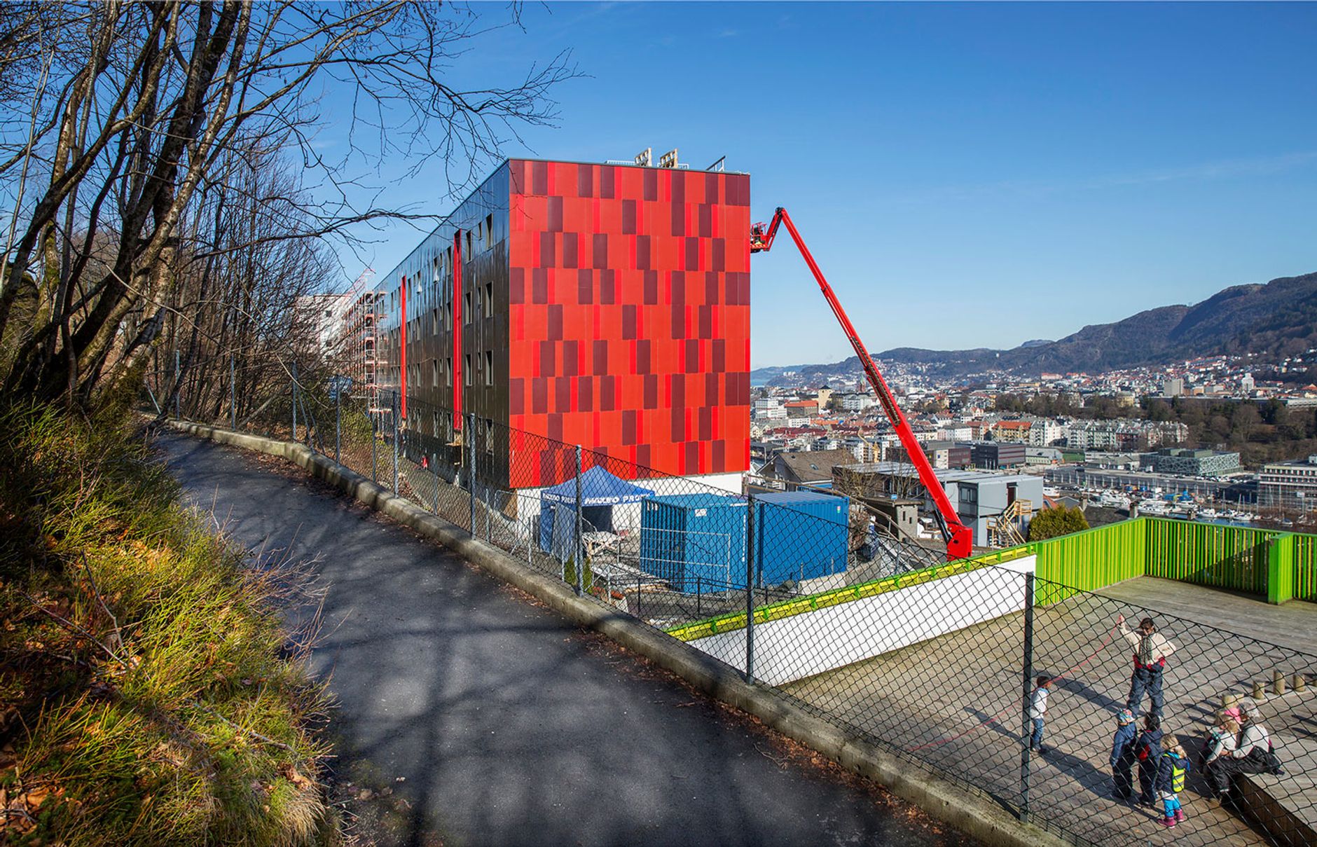 a red building with a crane on top of it is surrounded by trees and a chain link fence .