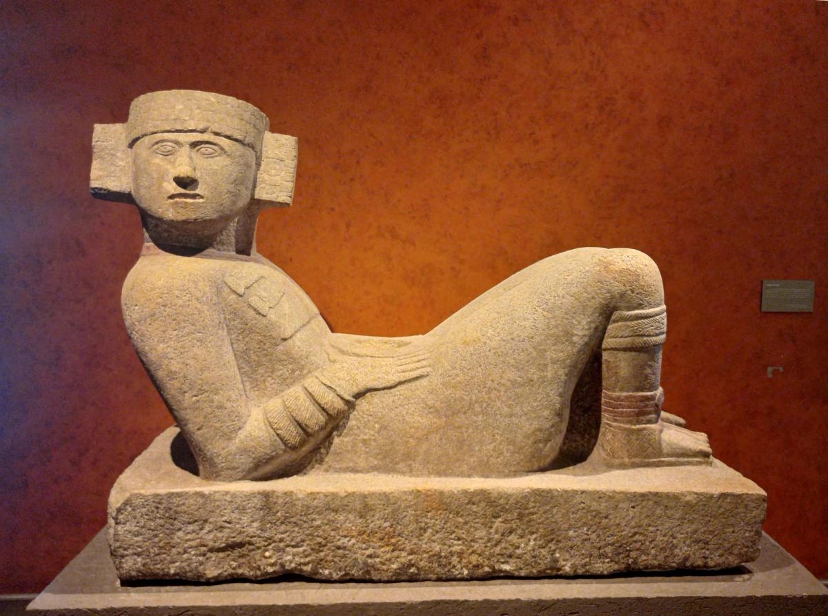 A reclining stone figure with its head turned sharply to one side, hands holding a dish on its belly.