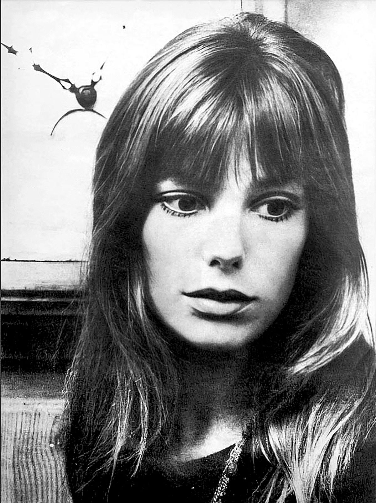 A black and white photograph of Jane Birkin in 1970, facing the camera with long hair and a fringe, in a plain dark top.